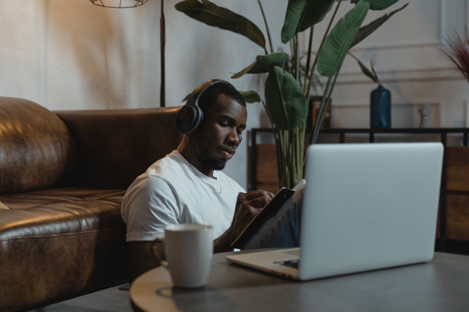 A learner wearing headphones taking notes beside a laptop