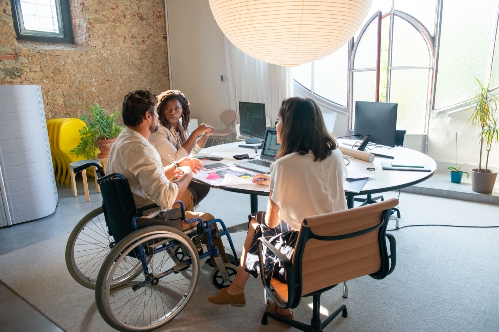Three colleagues, including a wheelchair user, collaborating around a table with laptops