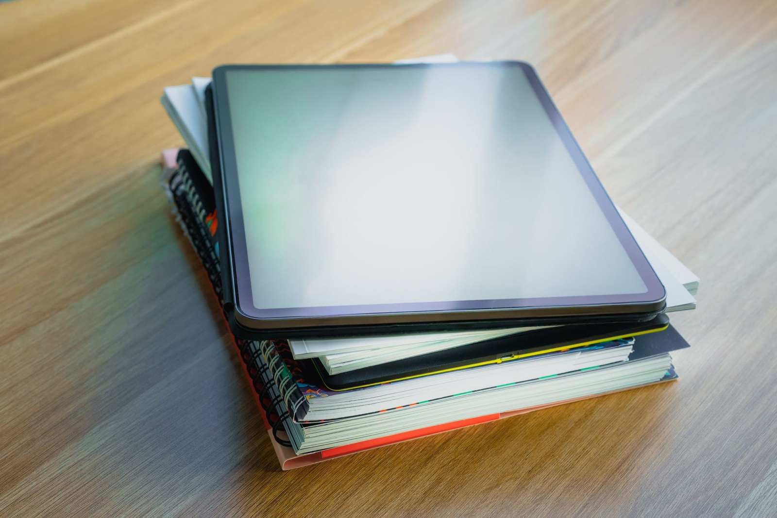 A blank digital tablet resting on a stack of books and notebooks
