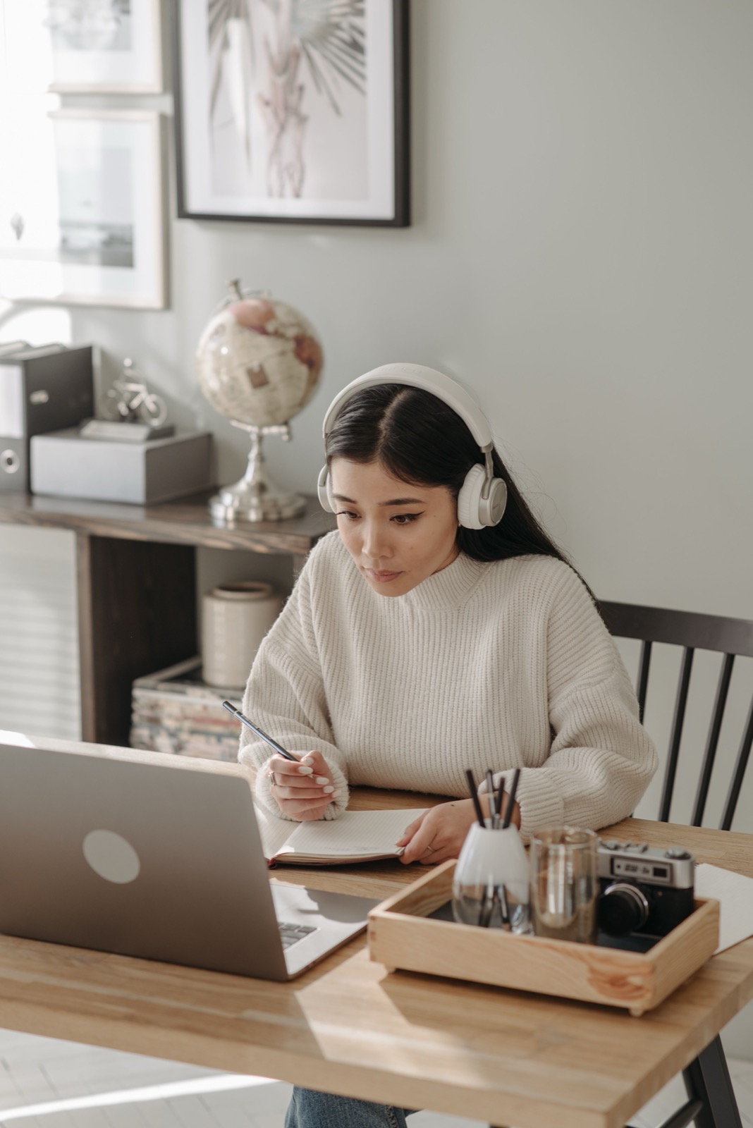 A learner wearing headphones taking notes beside a laptop