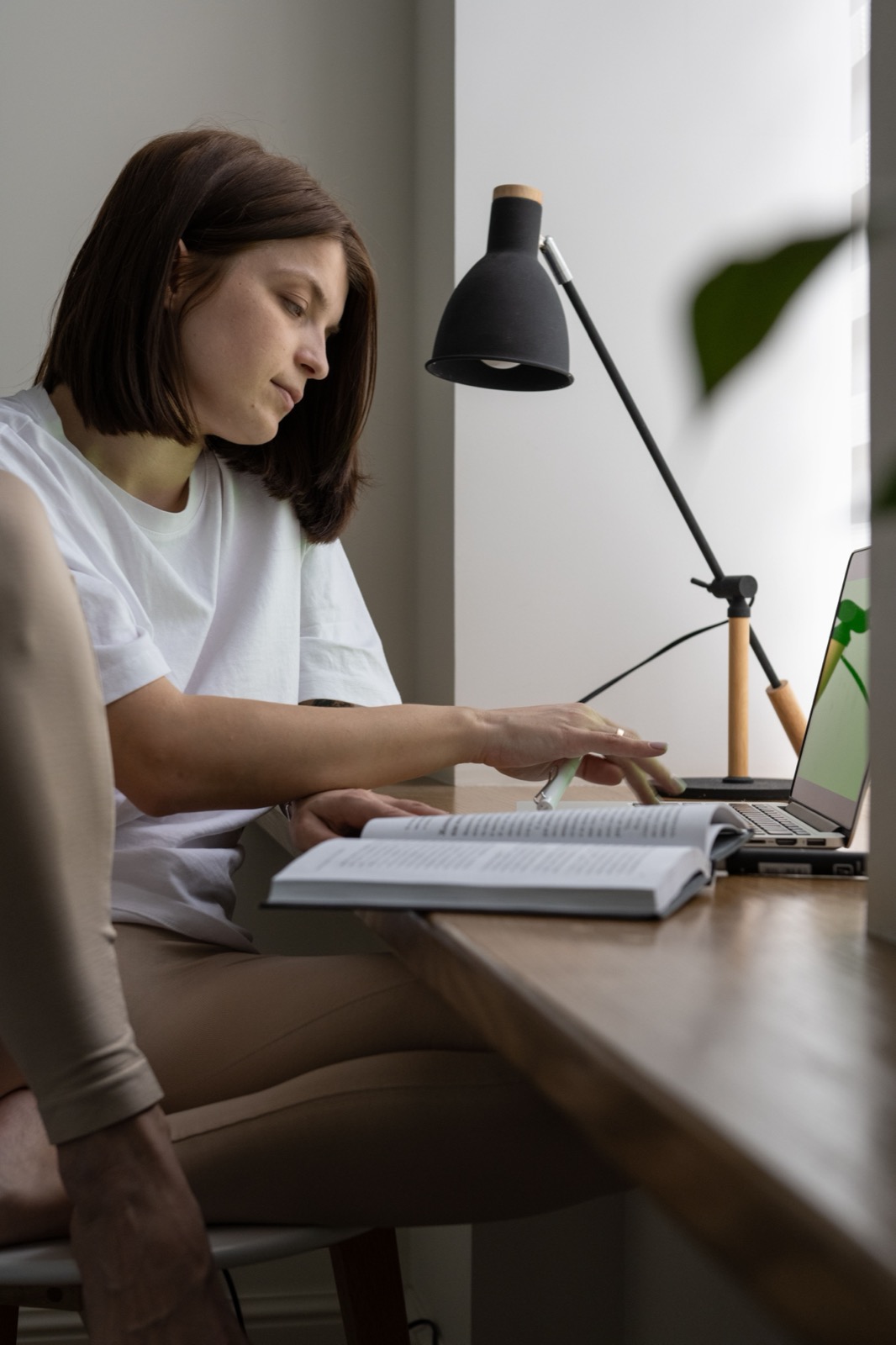 An editor consulting an open book while working on a laptop
